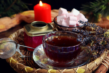 Winter still life: a cup of tea with a bouquet of lavender against the background of a burning candle, pine branches and a vase with airy marshmallows, close-up