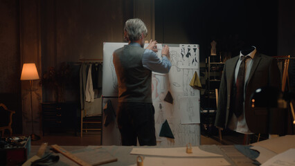 Male mature tailor in luxury designer atelier or tailoring studio. He works with sketch of future...