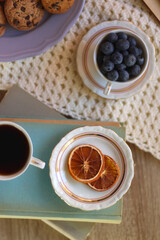 Plate of cookies, cup of tea, fresh blueberries, dry oranges, stack of books, reading glasses and tablet on the table. Hygge at home. Flat lay.