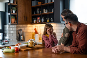 Young little girl standing in the kitchen with her parents looking at her mom's belly thinking about how wonderful it would be to have a baby sister to play with.