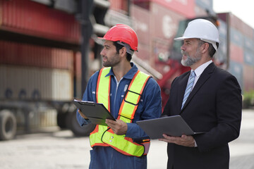 Industrial worker works with co-worker at overseas shipping container yard . Logistics supply chain management and international goods export concept .