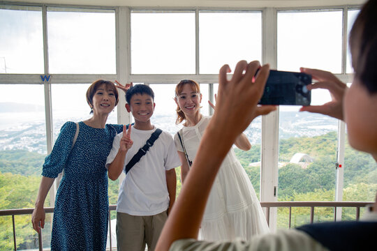 A boy using his mobile phone to take a picture of three people, a 13 year old boy, his mother and a friend.