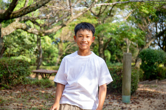 A 13 year old boy in a white teeshirt, smiling, outdoors in a park.