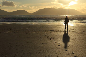 Silhouette of a person standing with their shadow behind them on the beach looking towards the...