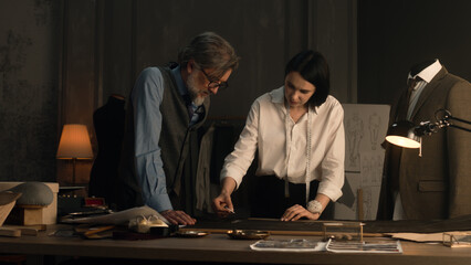 Male and female tailors working on sketch pattern of business or wedding suit. Mannequin with...