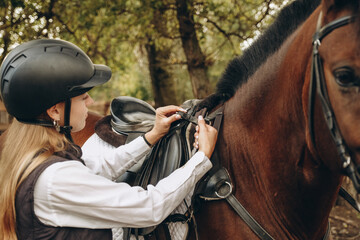 A young woman jockey adjusts the harness on her horse before training.