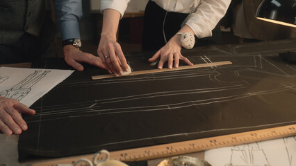Male and female tailors transfer the sketch of future clothes to the fabric. They use ruler, soap...