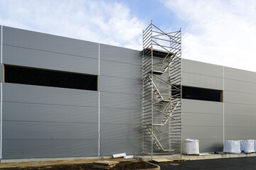 Gray sandwich panel facade of a unfinished warehouse building, tubular multilevel scaffolding