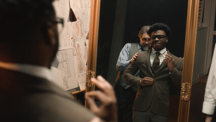 African American man on suit fitting in stylish designer atelier or in dim luxury clothing shop....