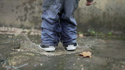 Child jumping into water puddle. Toddler wearing boots splash into puddle4
