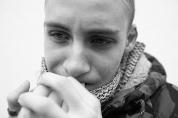 A young man in a military jacket nervously bites his nails