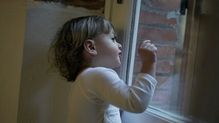 Child boy standing by window pointing at something outside