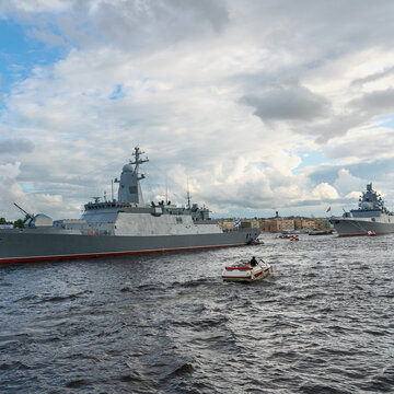 tourists on a pleasure boat take pictures of a warship parked on the river in the center of the city of St. Petersburg, Russia
