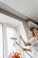 Housekeeper is spraying detergent and cleaning window at home. Housewife woman is cleaning at home...