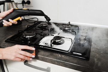 Woman cleaner is steaming and disinfecting cooker in kitchen. Girl worker of domestic cleaning service clean using vapour machine. Steam cleaning of kitchen using professional steam generator.