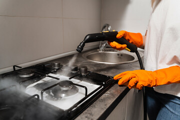 Steam cleaning of cooker in kitchen close-up. Worker of cleaning service is steaming on cooker...