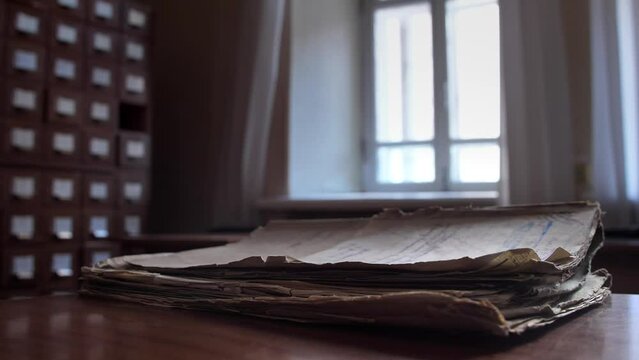 The wind shakes the pages of a vintage archival document. A close-up of a folder with old documents lies on a table in an archive or file cabinet building.