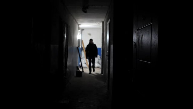 Slow motion silhouette of a stranger who walks along the corridor of an old abandoned building comes to the door and opens it. Backlit man walks through a long room. shadow of a man