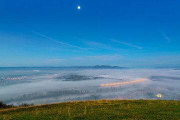 Aerial view of the town in the early morning mist is beautiful in the highlands. Low clouds and fog cover the sleeping city, photo in full moon light. Alpine mountain valley mists landscape at dawn