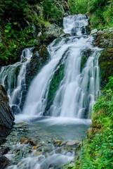 Beautiful mountain rainforest waterfall with fast flowing water and rocks, long exposure. Natural seasonal travel outdoor background with sun shining. Stream waterfall on rocks in the forest