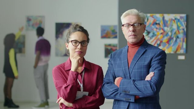 Portrait waist up shot of female gallery curator and senior male artist standing in exhibition hall and posing for camera