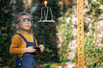 Portrait of little boy with remote control crane beam in an industrial warehouse. Little boy...