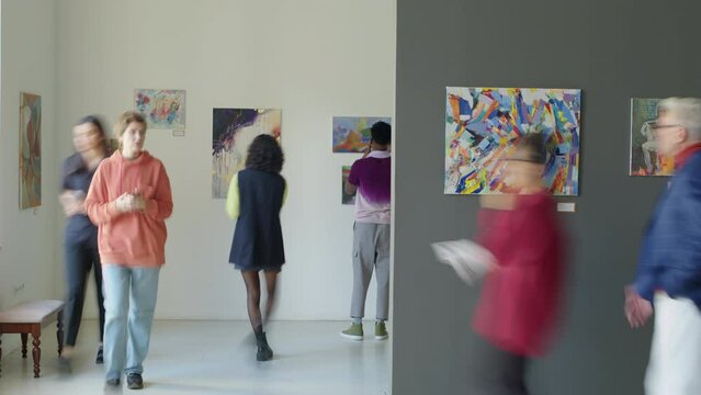 Time lapse of people walking in exhibition hall and observing contemporary paintings while visiting art gallery