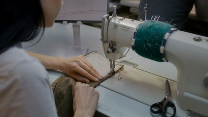 Female seamstress or dressmaker sits at sewing machine and works with elegant wedding suit. Tailors sketch displayed at the screen of tablet. Atelier workshop. Concept of fashion. Close up shooting.