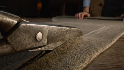 Close-up shot of tailor cutting fabric according to sketch using scissors for sewing. Process of...