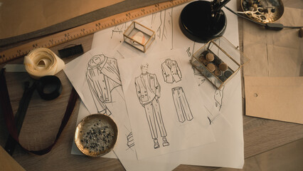 Fototapeta na wymiar Cinematic shot of table with drawings, needles, threads, buttons, ribbons, soap and ruler. Sketches of clothes, suits and jackets. Designer atelier or tailoring studio. Fashion and hand craft concept.