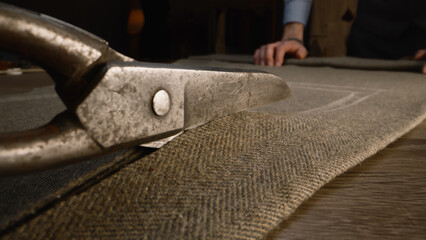 Close-up shot of tailor cutting fabric according to sketch using scissors for sewing. Process of...