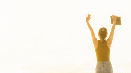Back view of a woman raising both hands in the fresh morning air with golden light.