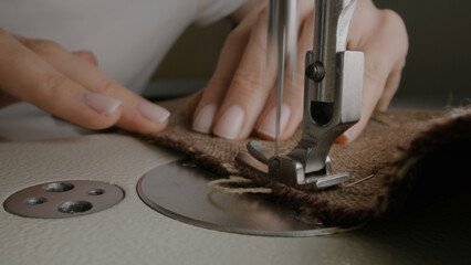 Hands of female seamstress works on sewing machine. Designer sews fabric in atelier sewing workshop. Concept of small business, tailoring industry, hand craft and fashion. Macro