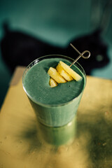 green spirulina smoothie with pineapple on brass, gold table and teal background with black cat