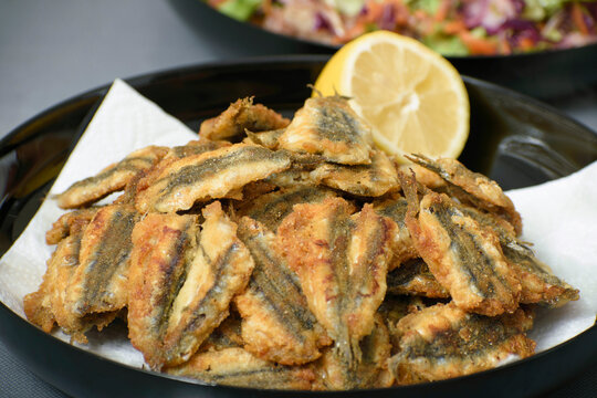 Pan fried anchovy fish in a plate with lemon on the side