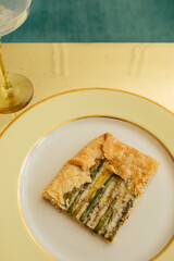 single serving, rectangular slice of an asparagus gruyere galette on golden yellow plate with yellow stemmed glassware