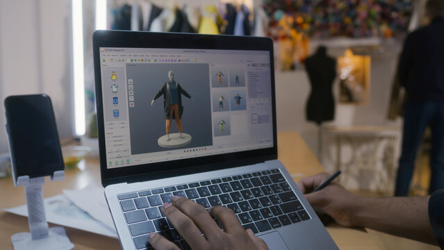 African American fashion designer creates clothes in 3D modeling software on laptop using digital tablet and stylus. He works in atelier workshop. Concept of fashion and technologies in business.