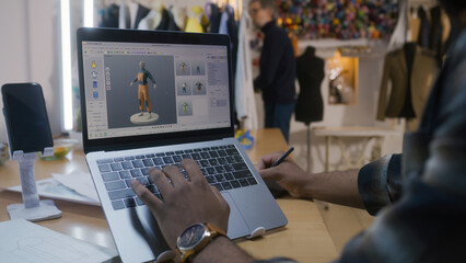 African American fashion designer creates clothes in 3D modeling software on laptop using digital...