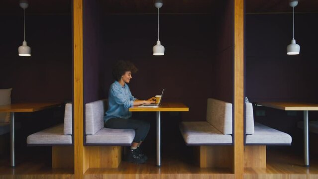 Profile view of businesswoman working at table in seating area of modern office with takeaway drink - shot in slow motion