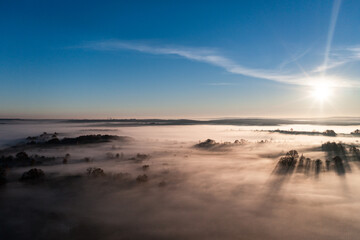 Flying over a village at dawn, bright sun on the horizon and fog over a small village.