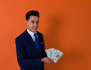 waist up image of a latin elegant man holding US dollar bills while smiling ahead an orange background