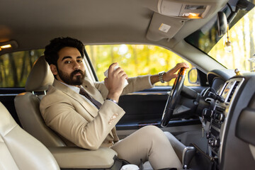 Smiling arab businessman driving a car while drinking coffee