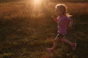 Fototapeta na wymiar A girl of four years old runs in a field against the background of an orange sun at sunset, active recreation.