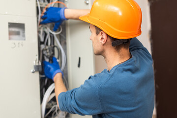 Close up shot of hand of aged electrician repairman in uniform working, fixing, installing ethernet cable in fuse box, holding flashlight and cable. hand and cable