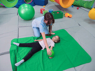 Physical therapist working with little girl in sensory room. Exercising with weighted ball and...