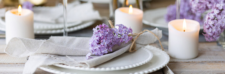 Obraz na płótnie Canvas Beautiful table decor for a wedding dinner with a spring blooming lilac flowers. Celebration of a special event. Fancy white plates, and wineglasses. Countryside style. Banner