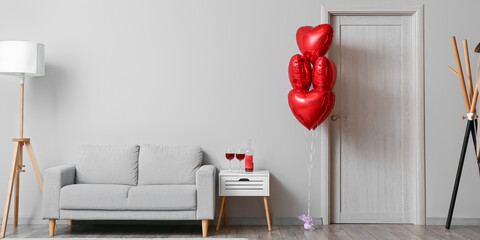 Interior of living room with red heart shaped balloons, table with wine and sofa. Valentine's Day celebration