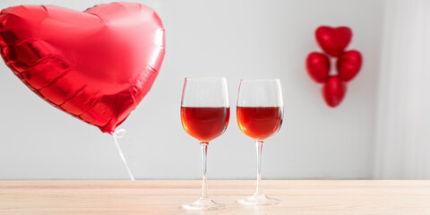 Glasses of wine on wooden table and heart shaped balloon for Valentine's day in room