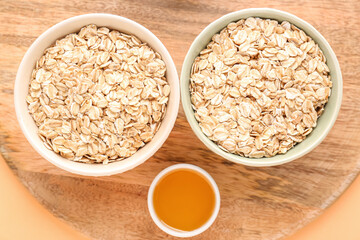 Wooden board with bowls of raw oatmeal and honey, closeup