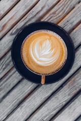 Top view on stylish latte coffee mug with flower art on wooden table background 